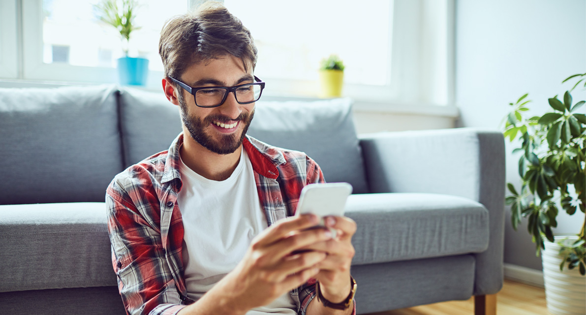 Man sitting on phone with back to couch holding smartphone