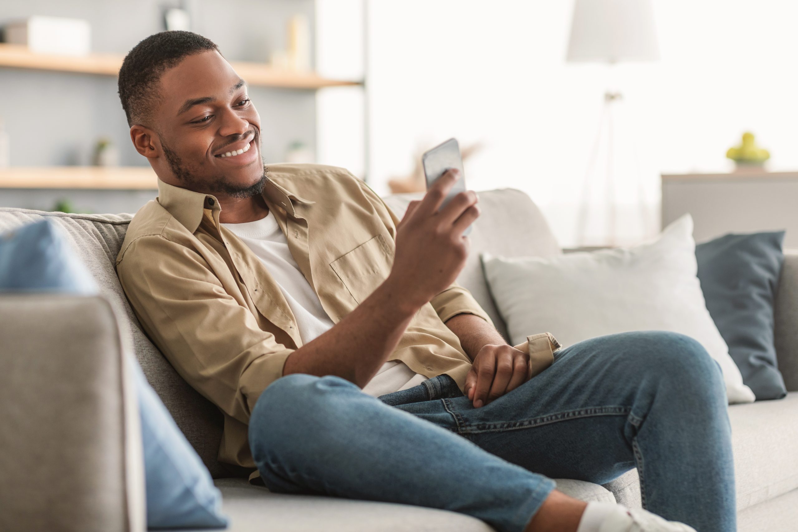 Side view of man sitting on couch using phone